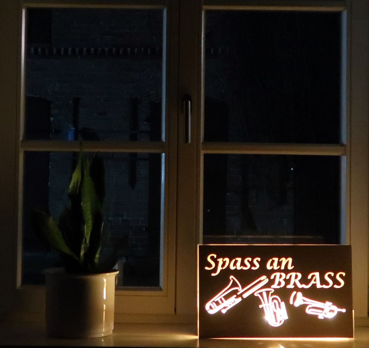 Foto: Ein leuchtendes Schild mit dem Logo des Bläserensembles Spass an Brass steht auf einer Fensterbank.